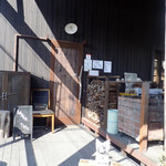 菜菜cafe - 薪ストーブなどで使う薪が積んであったりだけど、小ぎれいな入り口ミャ