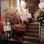 焼鳥・元気 - 階段の半分ぐらいは、お祝いのお花ですよ。 すごいですよね。 少し階段を登るとお店の入口です。 ここは、和風な感じで、横にガラガラって開けるタイプですね。 お腹もペコペコです。 さあ、入店しましょう。