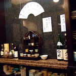 旬彩　和 - カウンター奥、食器類、酒類。中央は日本酒注文時に選べる各種ぐい飲み