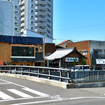 お好み焼き屋 とみ - 駅前に立つと，川の向こうに看板が見えます