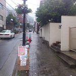 クスム本場家庭料理 - 新）旧店舗があった葉山ハイツ前にも新店を案内する看板が設置されています。ちょうどこの写真の山手左側に見える茶色い建物が異人プラザです