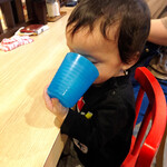 拉麺大公 - ベビーチェアでコップをハミハミする我が子