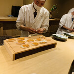 富小路 やま岸 - ◎お弟子さんが、平貝の上にこのこを乗せ、その上に焼いた献上餅を伸ばして乗せていく。