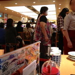 Mawashizushi Katsu Katsu Midori - テーブル席から回転寿司のカウンターを見たところ。手前に順番待ちの人たちが座っています。
