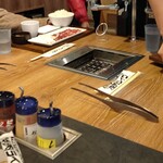 Yakiniku Raiku - テーブルに半分埋まっている形での縦一列での設置。 調味料の容器は、注ぎ口だけが蓋の上部に細長い管で伸びている形態。 これって、遠方の調味料を取るとき、気をつけても袖や手が蓋から伸びた注ぎ口に触れてしまう場合が多い。