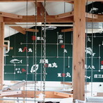 平塚漁港の食堂 - ２階入口（134号線側）から入ると階段の踊り場からは、魚の絵や釣り船屋さんの名前が書かれたグリーンボードが見えます。