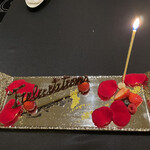 ガストロノミー ジョエル・ロブション - 金色の装飾やバラの花びらが添えられたデザートプレートに、「Congratulations」の文字とキャンドルが灯され、特別な瞬間を華やかに演出する一皿。