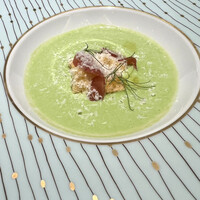 シェ・イノ - グリンピースの冷製ポタージュ生ハムとサクサククルトン、羊のチーズがふりかけられ、グリンピースのスプラウトがトッピング　初夏にふさわしい味わいのスープ