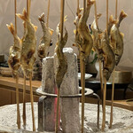 銀座 しのはら - 大きな囲炉裏の鉢に鮎の串刺しが11本
      突き刺さって並んでおります。
      贅沢な事に二尾のご用意で
      小さい方が琵琶湖産で
      大きい方が郡上八幡長良川の鮎です。
      この2種を食べ比べさせてくれるご用意