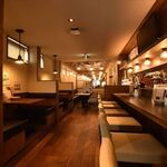 洋風ダイニングバー 町家バル - 内観写真:入口から奥へと伸びる1階フロアは、木の温もりを感じる落ち着いた空間。カウンター席とテーブル席をバランスよく配置し、お一人様から少人数まで幅広く対応しています。オープンキッチンを眺めながら過ごせるカウンターと、視線や動線に配慮した配置で、賑わいの中でもゆったり過ごせる1階席です。