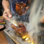 焼肉 肉萬 - 秘伝のタレをつけて焼いてるところ