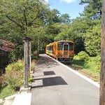 赤い屋根の喫茶店 駅舎 - 桜のトンネルの向こうからオレンジ色列車が。左の赤い屋根が“駅舎”です。看板の所がホーム側の出入口になっています。