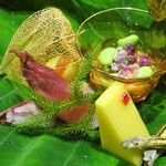 草喰 なかひがし - 八寸：透かしほおずき 卵黄の味噌漬を挟んだ銀杏、玉蜀黍の寒天、酢飯を詰めた茗荷の酢漬け、無花果と枝豆のきな粉酢和え、ごり、味女、ウドの花、のし梅を挟んだ里芋、キハダ、鮎のテリーヌを包んだ花オクラ