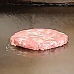 エイチズバーガー スタンドアンドバー - 注文をすると鉄板にパティを投入。
            画像が荒いので分かり難いのですが、牛肉100%のパティはかなり粗挽な肉で脂も塊がまだらに混ぜ込まれています。