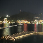 でん助茶屋 - 今回の席からの景色　肉眼だともっと良く見えます。サンビーチの防潮堤の向こうは、左からアカオ、後楽園ホテルとフーア、上の光は熱海城です。右の方は、ホテル群です。