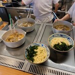 丸亀製麺 - 鍋に入ったアサリが茹でられています。出来上がったアサリは手前のうどんに乗せて出来上がりです