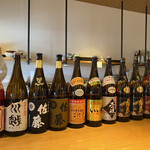Uotora - 日本酒がカウンターに陳列され、奥の棚には常連方のボトルキープもある。