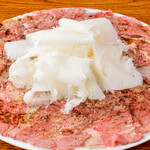 Beef carpaccio spread all over the plate, topped with fluffy cheese