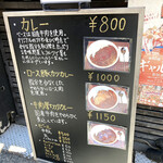 カルダモン． - 店頭にはメニューの書かれたボードが置かれている。価格差を考えると「カレー」よりも「ロース豚カツカレー」や「牛肉厚切りカレー」を選ぶ方がお得感はある。