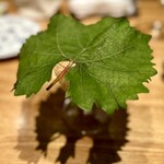 やまぐち - ❷干し貝柱の出汁ゼリー ～大きな葉に隠れた干し貝柱の出汁にスライスした干し海鼠とナガノパープル、焼き茄子を添えた一品。干し貝柱のだしのゼリーとナガノパープルという果実を上手く使った料理が夏らしい。