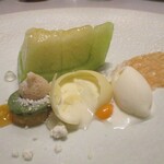 レミニセンス - 天使音メロン：浜松の天使音メロン（アマネ）を中心に、抹茶ソースのメレンゲ、ホワイトチョコレートに包まれたメロンのソース、バニラアイスが並び、薄い板状のカラメルが飾られています。 球体のホワイトチョコの真ん中にナイフを入れ 半分に割ると、中からメロンのソースがトロォ～リと流れ出ます。