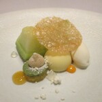 レミニセンス - 天使音メロン：浜松の天使音メロン（アマネ）を中心に、抹茶ソースのメレンゲ、ホワイトチョコレートに包まれたメロンのソース、バニラアイスが並び、薄い板状のカラメルが飾られています。 球体のホワイトチョコの真ん中にナイフを入れ 半分に割ると、中からメロンのソースがトロォ～リと流れ出ます。