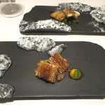 レミニセンス - 鰻：鰻を白焼きにしてから ワインを使用しフレンチテイストに仕上げた三河一色産の鰻は、炭火でパリッと焼きあげられた皮の食感と香ばしさ、ウナギ本来の美味しさが熱々・最高の味わいで堪能できます。鰻の下には、牛のタルタルと 香りづけに棒葉が敷かれ、胡麻・赤ワインのソースで 鰻の美がさを更に引き立てています。 脇には うずら卵の黄身が添えられています。