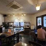 こふじもち 横川店 - 店内はクリーム色の壁に濃茶色の木製調度品、少し落ち着いた雰囲気がありますね
            持ち帰り販売カウンターがあります
            お席はテーブル6席×1卓、テーブル4席×2卓の合計14席