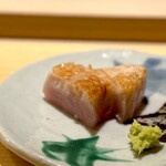 すし処 めくみ - ブリ。 サラシで丁寧に包まれて10日熟成させたブリを取り出し、本当に大事そうに削ぎ、カットし、直前に炭火で炙り供されます。 ブリは比較的長く熟成されますが、この個体は、熟成後はキレイなピンク色に染まってました。 色を見るだけで食欲が爆発しそう。 甘く、深く、舌で押しつぶせるほどに柔らかく、口の中に上質な脂と熟成の旨味があふれだします。 味付けは塩のみ。 これがめくみの技です。