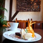 Kohakukan - 重厚感ある銅色の壁掛け、爽やかなオレンジが立体感を演出するチョコレート色の一皿、そしてコーヒー色で満たされた背の高いカップの対比が印象的だ。