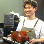 小菜一碟 - こんがりと飴色に焼きあがった北京ダックを手にする 吉田シェフ。