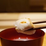 炎水 - トロみのあるコクとグッと立ち上がるふぐヒレの香ばしさ！ 焼き白子をパツんとほどけばミルキーな味わいとふぐ出汁の旨味が香りと一体になり、綺麗な重奏をつくる。 お雑煮に見立てた綺麗な先付けです。