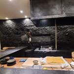 Sakamotoya Ichibee - 店内は黒塗りの岩盤を模した板場の後ろ壁&客席側の白壁とのコントラストがモダンでスタイリッシュな空間を生み出しています
                黒塗りのL字カウンター、木製の板場との組み合わせによりモダンさの中に和みを演出