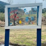 きままな台所 - 可愛い看板の背景には山々と小川が