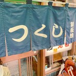 つくし - 店の外には、緑のれんと黄色い看板が掛かっていた。
      看板には、「つくし　もんじゃ焼き」と書かれていた。