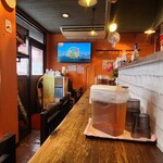 鉄板居酒屋 たちまち - 店内は橙色の壁、煉瓦色のコンクリート床、木製カウンター、年季は入っていますがクリンリネスがなされており、居心地は良いです
            BGM代わりにテレビ音声が流されています
            お席はコ字カウンター10席のみ