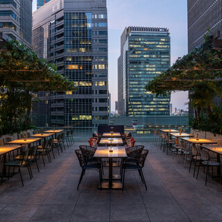 Open terrace seats full of greenery with a night view of Tokyo's cityscape and buildings.