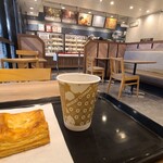 ミスタードーナツ - 店内はクリーム色の天井&壁(一部木板張り壁)、クリーム色でマーブル柄のPタイル貼り、ナチュラルウッドカラーのテーブル&椅子、白とグレーのギンガムチェックの長ソファ、穏やかな雰囲気