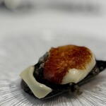 ウシマル - イカスミを練り込んだ真っ黒な自家製パンに、オリーブオイルで炒めた ゲソのぶつ切り、その上にこれはモッツァレラチーズでしょうか？ 手で持って一口でどうぞ、と。 イカゲソとチーズ、こんなに相性がいいとは！