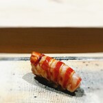 すし宮川 - クルマエビ。 宮川さん独特のフォルム。 尻尾はドコ行ったの？　って思ってたら、ちゃんとお腹の中にある。 フォルムすら品格を感じさせる。 弟子くん１が剥き、弟子くん２が切り整え、大将が握る。 臨場感が旨さをバク上げ。 旨いですねー。 ずっと咀嚼していたい。 これ一貫で一合飲めそう。