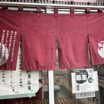 魔界ラーメン 月光 - 入り口の暖簾には「蝸牛が一生かけて歩む道のりを僕らは何歩で超えるのか。宇宙がくしゃみを一つする間に僕らは何度生まれ変わるのか。」というメッセージも