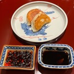 KOBAYASHI - カウンター厨房で盛り付けられた焼餃子。左の薬味は自家製の食べるラー油、右手は生姜入りの黒酢醤油です
