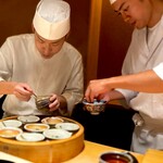 くるますし - 鮎の蒸し鮨。 でっかい蒸籠から出てきたのは・・ 大将が大急ぎでソースをかけ、弟子くんも 大急ぎでアオサをのせ、大急ぎで客の前に。 二人の連携はすっかり板についた感じ。 よほど熱々で食べさせたいらしい。