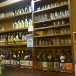 粗肴 - 棚に並ぶ焼酎と田酒のTシャツを着た若大将