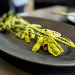 Txispa - 続いて、厨房レベルにあるアイランドテーブルで、シェフの説明を聞きながら、熾火で火入れした獲れたて枝豆を、立ったままいただきます。
                                味わいもスタイルも、新鮮！