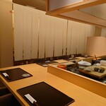 佳肴 三佐和 - 清潔感のある店内。L字のカウンター席は全7席。手前4席の端2席に座る。料理人の仕事ぶりを拝見できる席だ。布製の間仕切り越しに見え隠れするテーブル席は12席ほど。