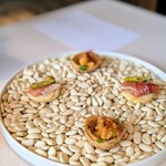 古我邸 - 天使エビのフリットと、生ハム　コカ。生ハムはししとう？唐辛子？のピクルスでピリ辛、オリーブを乗せて。天使エビのフリットの器はまあるくて、春巻きの皮を揚げたような薄くてパリパリの器。