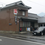 手打うどん たむら - 道路をはさんさんで駐車場側から撮りました。車の後ろの白い建物がお店です。