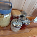 肉汁うどん いちだ家。 - カウンター上の薬味。天かす、一味、コショウ、ラー油、にんにく