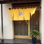 おかめ寿司 - この日は風が強かった。梔子色？の暖簾が清々しい